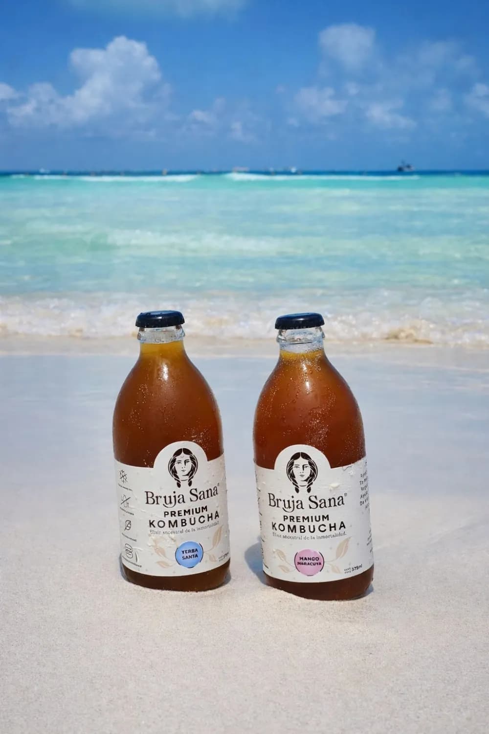Two Bruja Sana bottles on a Tulum beach